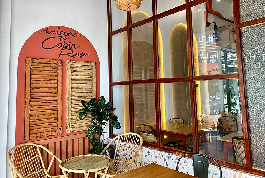 Mural 'Welcome to Cabin Rose' dan kerusi rotan di ruang dalam kafe
